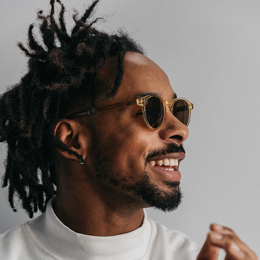 Black man wearing round yellow frame sunglasses facing sideways